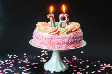 Üzerinde mumlar olan pembe bir doğum günü pastası masasında renkli konfetilerle çevrilidir..