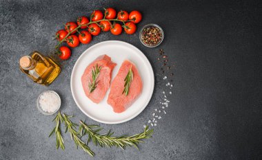 Beyaz seramik tabakta çiğ biftek, domates, tuz ve biber.