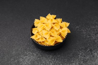 Koyu arkaplanda siyah bir kasede sergilenen pişmemiş farfalle makarnası..