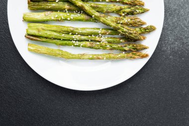 Taze ızgara kuşkonmaz mızrakları beyaz bir tabakta susam tohumlarıyla kaplıdır..