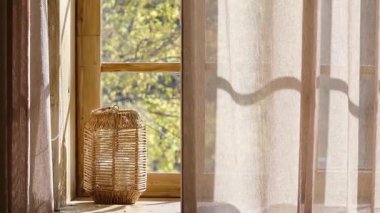 Pencere kenarında örülmüş bir fener, sonbahar yaprakları ahşap pencere camı ve katıksız perdeden görülebiliyor.