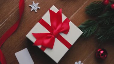 Kırmızı kurdeleli beyaz hediye kutusu, kar taneleri, çam dalı ve ahşap yüzeyde takı.