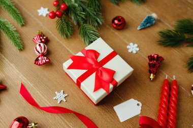 Kırmızı fiyonklu hediye kutusu Noel süsleri ve ağaçta çam dallarıyla çevrili.