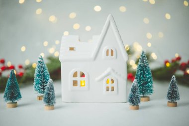 Küçük seramik ev ve dekore edilmiş arka plan ışıkları olan çam ağaçları.