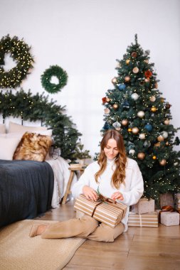 İçerideki süslü Noel ağacının yanında çizgili bir hediye açan kadın.