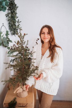 Samimi beyaz hırkalı kadın, kapalı alanda çuval bezi tabanlı küçük yeşil bir ağaç hazırlıyor..