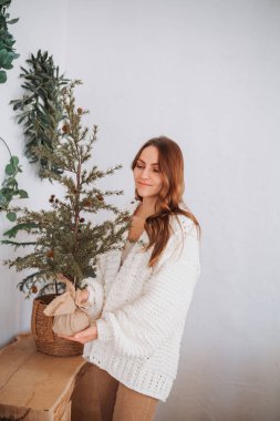 Küçük çam ağacını tutan bir kadın doğal sicimle süslenmiş ve ahşap masa üzerinde çuval bezi olan.