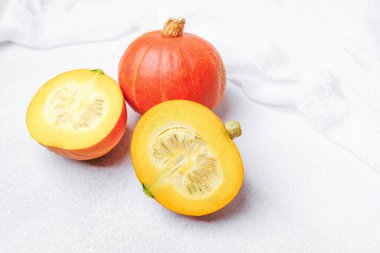 Turuncu balkabakları beyaz kumaş detaylarıyla dokulu beyaz bir yüzey üzerinde sarı et ve tohumlar ortaya çıkarıyor.