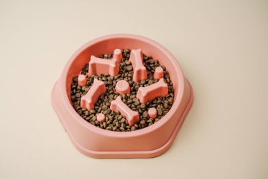 Pembe yavaş beslenen köpek kasesi hafif arka planda köpek mamaları ve kemik şekilleriyle dolu..