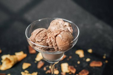 Bir kepçe çikolatalı dondurma ve siyah yüzeyde waffle kırıntılarıyla dolu cam bardak.