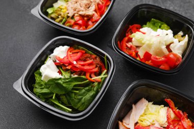 Restoran teslimatı ya da yemek hazırlama konsepti için siyah kaplarda taze sebzelerle karışık salatalar et peyniri ve yeşillikler.