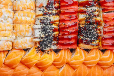 Suşi ruloları, somon balıklı karides ve siyah tabakta servis edilen yılan balıklı.