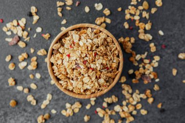 Üst manzara granola kasede, koyu arkaplanda dağınık parçalar var.