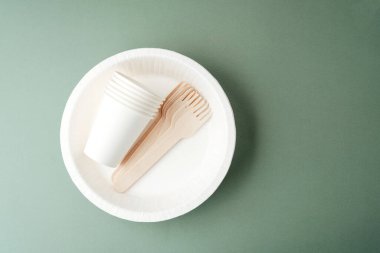 Tek kullanımlık beyaz bardaklar ve yeşil arka planlı ahşap çatallar.