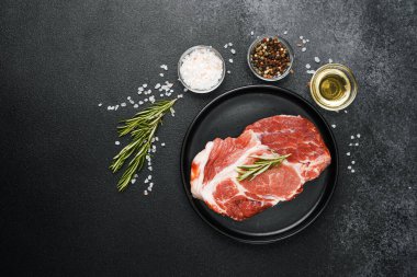 Çiğ biftek, otlar ve siyah tabakta baharatlar.
