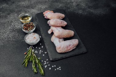 Siyah tahtada çiğ tavuk kanadı ve baharat.