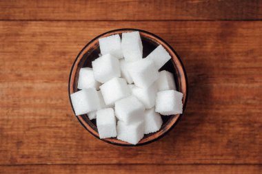 Şeker küpleriyle dolu bir kase ahşap bir yüzeyde duruyor, tatlandırmak için mükemmel..