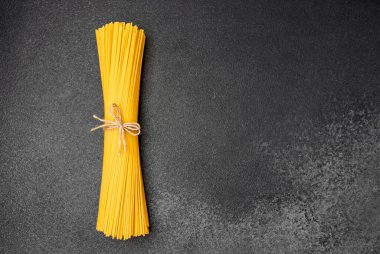 Koyu arkaplanda iple bağlanmış pişmemiş sarı bir makarna demeti..