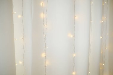 Sıcak sicim ışıkları narin beyaz perdelerin üzerinde hafifçe parlıyor, rahat ve büyülü bir ortam yaratıyor..