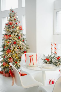 Kırmızı kurdeleli beyaz Noel ağacı ve pasta ve mumlarla süslenmiş ışıklar.