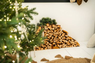 Odanın içinde sıcak ışıkları ve odun yığınlarıyla süslenmiş her yeri yeşil ağaçlar.