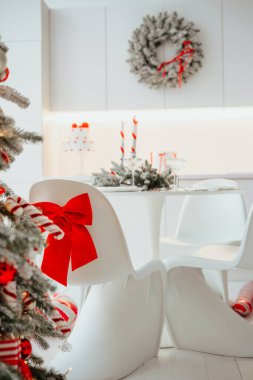 Kırmızı kurdeleyle süslenmiş Noel ağacı, Noel süsü ve sandalyeli yemek masası.