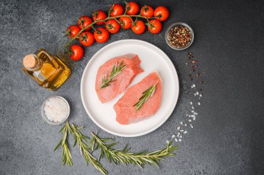 Beyaz seramik tabakta çiğ biftek, domates, tuz ve biber.