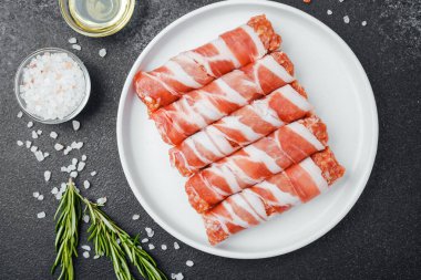 Çiğ domuz pastırması beyaz tabağa sarılmış, baharatlı ve otlu.