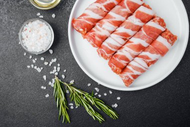 Çiğ domuz pastırması beyaz tabağa sarılmış, baharatlı ve otlu.