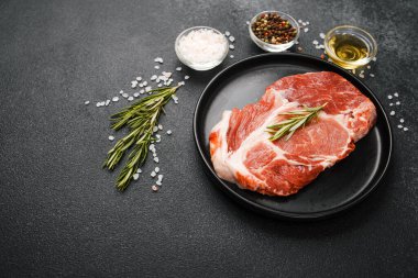 Çiğ biftek, otlar ve siyah tabakta baharatlar.