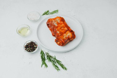 Beyaz tabakta marine edilmiş domuz pirzolası, biberiye ve baharatlı.