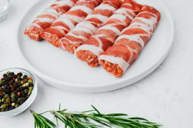 Jambona sarılmış sosis, beyaz tabakta otlar ve yağla birlikte.