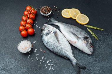 Domatesli taze çiğ dorado balığı limon ve siyah arka planda baharatlar.