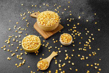 Kırsal yemek hazırlığı, diyet ya da malzeme konsepti için taştan arka planda sarı bezelyeli çoklu ahşap kaseler ve kaşık.