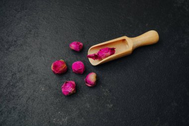 Koyu yüzeyde kurumuş gül tomurcukları, ahşap kepçeyle.