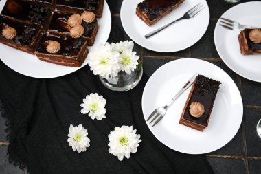 Çatallı, beyaz çiçekli, koyu renk kumaşlı beyaz tabaklarda çikolatalı pasta dilimleri.