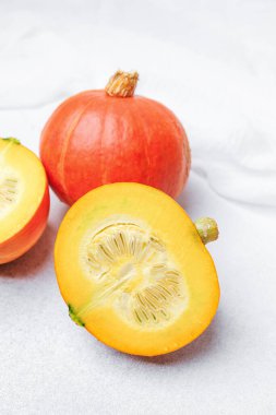 İki turuncu balkabağı bir kesik yumuşak beyaz kumaşla dokulu bir yüzeyde tohumları ortaya çıkarıyor.