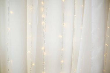 Yumuşak beyaz kumaş perdeleri ve arkasında parlak peri ışıkları var.