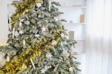 Beyaz süslerle süslenmiş yeşil köknar ağacı ve parlak bir odada sarı ışıklar.