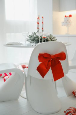 Kırmızı kurdeleli beyaz sandalyeler mum dolu bir Noel yemeği partisi için süslenmiş.