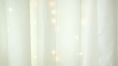 Yumuşak beyaz kumaş perdeler ve asılı peri ışıkları yumuşak bir parıltı ve rüya gibi bir atmosfer yaratıyor..