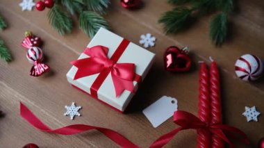 Kırmızı kurdeleli bayram hediyesi kutusu, çam dalları, kırmızı kalpler, şekerler ve kar taneleri.