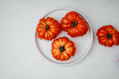 Dört kaburgalı aile yadigarı domates beyaz bir tabakta su damlacıkları ve parlak kırmızı organik ürünlerle otururlar.