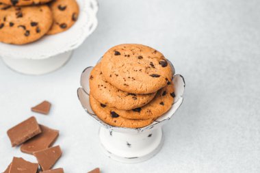 Çerezler düzgün bir şekilde bir kaseye istiflenmiş, hafif bir yüzeyde çikolata parçalarıyla çevrili..