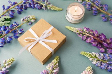 Yeşil arka planda lupin çiçekleri olan hediye kutusu ve mum.