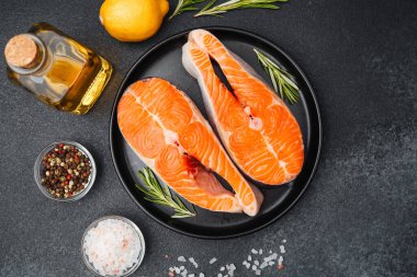 Parlak somon filetoları siyah bir tabakta dinleniyor. Yanında bitkiler ve limon dilimleri var..