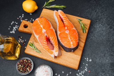 İki canlı somon filetosu ahşap bir kesme tahtasına otlar ve limonla oturur..