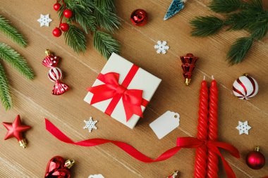 Noel hediyesi kutusu, kırmızı kurdele, mumlar, çam dalları, ahşap arka planda süsler.