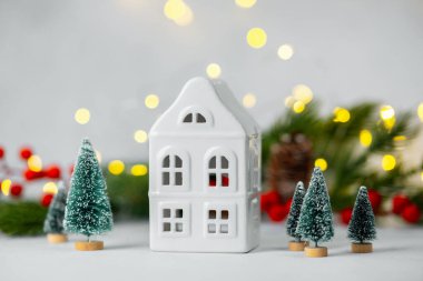 Beyaz seramik evli kış köyü sahnesi ve bayram ışıklarıyla süslenmiş küçük yeşil ağaçlar.