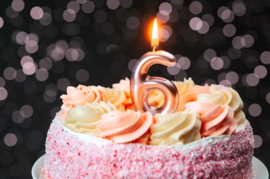 Pembe şekerle süslenmiş bir pasta ve altı numaralı şekle sahip bir mum..